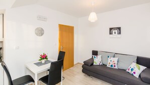 Un salon moderne avec un canapé gris, une table à manger avec deux chaises, une porte en bois et une horloge murale.