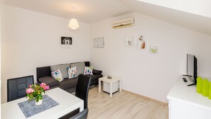 Un salon moderne comprenant un canapé, une table à manger avec des chaises, une petite table d’appoint blanche et un téléviseur posé sur un meuble.