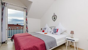 Une chambre à coucher comprenant un lit, une table de chevet, une commode, une fenêtre avec des rideaux et une vue sur un toit recouvert de tuiles rouges.