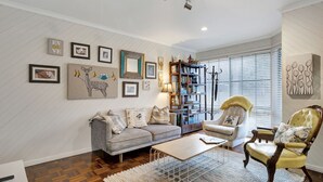 A living room with a sofa, armchair, and coffee table, a bookshelf, and various framed pictures on the wall. - Lauren's Place - This property is the perfect base for exploring all the region has to offer! (BRIGHT)