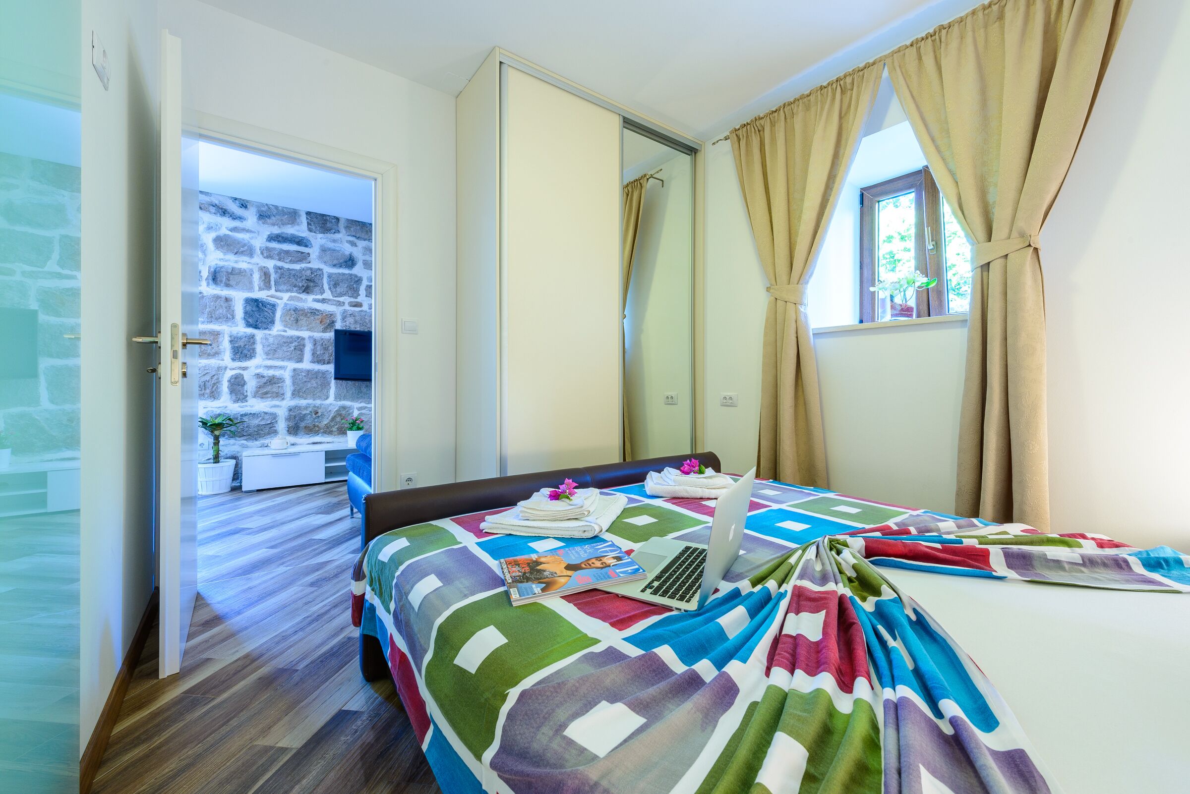 Ein Schlafzimmer mit einem Bett, einem Laptop, einer Steppdecke und einem Fenster mit Vorhängen.