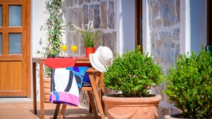 A wooden chair with a colorful blanket, a potted plant, and a glass of orange juice on a tiled patio.