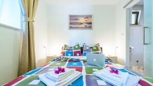 A neatly made bed with colorful bedding, a laptop on the bed, and a painting on the wall.