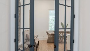 A room with a wooden floor, a dining table with chairs, and a window with blinds. - Massive Condo Sleeps 12 with Pool at North Beach (Tybee Island)