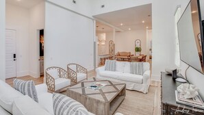 A spacious living room with a white sofa, two armchairs, a coffee table, and a dining area in the background. - Massive Condo Sleeps 12 with Pool at North Beach (Tybee Island)