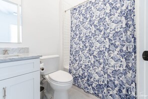 A bathroom with a toilet, sink, and shower curtain with a floral pattern. - Massive Condo Sleeps 12 with Pool at North Beach (Tybee Island)