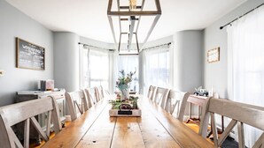 Uma longa mesa de jantar de madeira com cadeiras, um arranjo floral central e um lustre.