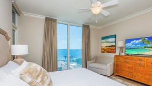 Habitación de hotel con una cama grande, televisión, cómoda de madera y vista al océano.