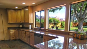 A kitchen with wooden cabinets, a granite countertop, and large windows offering a view of a landscaped garden. - Fabulous Red Rock Views, Private Outdoor Space, Hot Tub and Large Fenced Yard. (Sedona)
