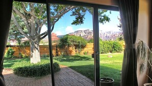 A room with a large sliding glass door leading to an outdoor area with a tree, grass, and a brick pathway. - Fabulous Red Rock Views, Private Outdoor Space, Hot Tub and Large Fenced Yard. (Sedona)