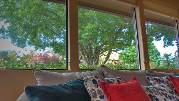 A room with a sofa and large windows offering a view of trees and a distant landscape. - Fabulous Red Rock Views, Private Outdoor Space, Hot Tub and Large Fenced Yard. (Sedona)