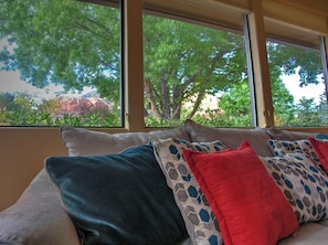 A room with a sofa and large windows offering a view of trees and a distant landscape.