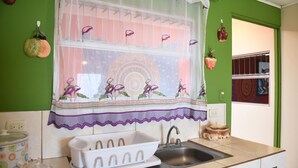 Une cuisine avec un évier, une fenêtre agrémentée d’un rideau décoratif et un mur vert.