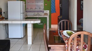Une cuisine compacte comprenant un réfrigérateur, une table à manger avec des chaises et une petite fenêtre avec un rideau.