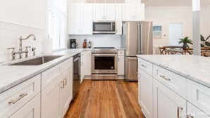A modern kitchen with white cabinets, stainless steel appliances, and a wooden floor. - 2 King Bedrooms in Historic Barracks at North Beach (Tybee Island)