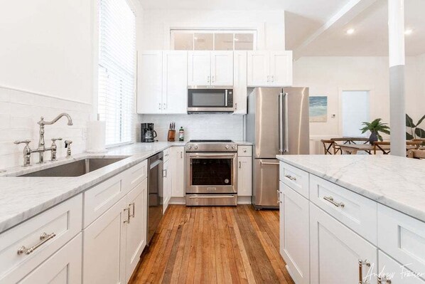 A modern kitchen with white cabinets, stainless steel appliances, and a wooden floor.
