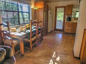 Une cuisine avec des meubles en bois, un réfrigérateur, une table à manger avec des chaises et une fenêtre donnant sur des arbres.