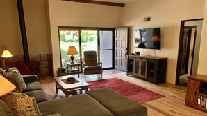 A living room with a sectional sofa, a wooden coffee table, a red rug, a television, and a sliding glass door leading to a patio.