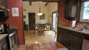 A kitchen with wooden cabinets, a tiled floor, a dining area with chairs and a table, and a window providing natural light.