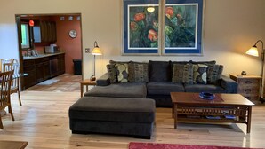 A living room with a sofa, ottoman, and coffee table, a dining area with chairs and a table, and a kitchen with cabinets and appliances.