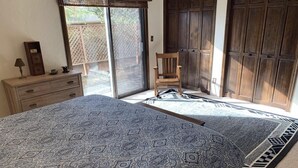 A bedroom with a large bed, a wooden chair, a dresser, and a sliding glass door leading to an outdoor area.