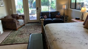 Ein Schlafzimmer mit Bett, Sofa, Sessel und Schreibtisch. Ein Fenster bietet Blick auf Grünflächen.