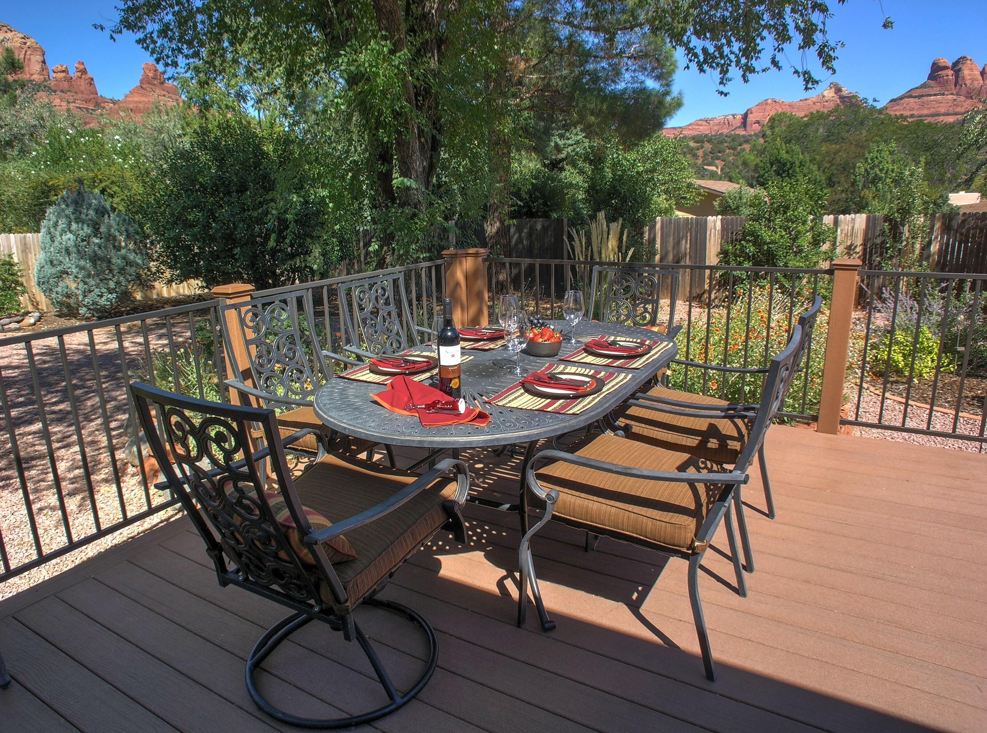 A round metal table with four chairs, set on a wooden deck with a metal railing.