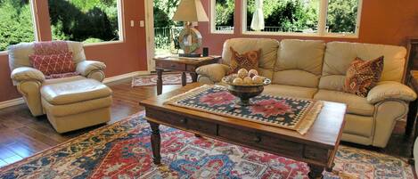 Un salon avec un canapé beige, un fauteuil assorti, une table basse sur laquelle se trouve un vase décoratif, et un grand tapis à motifs.