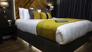 Een moderne hotelkamer met een groot bed, een nachtkastje met lamp en een paar slippers op de vloer.