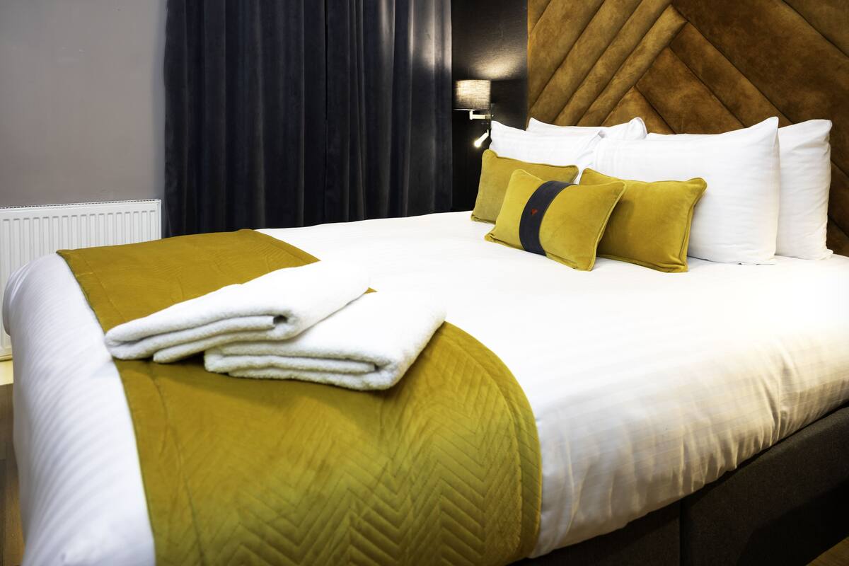 Een netjes opgemaakt bed met een geel-witte dekbedovertrek, witte kussens en een opgevouwen witte handdoek.