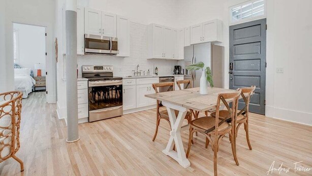 Een moderne keuken met witte kasten, een houten eettafel en rieten stoelen.