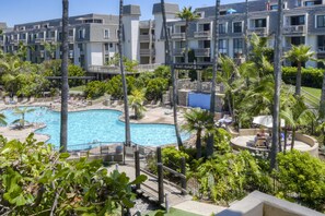 Um resort com uma piscina grande, palmeiras e um edifício com várias andares e varandas.