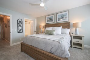 Een slaapkamer met een houten bed, twee nachtkastjes, een plafondventilator en ingelijste foto's aan de muur.