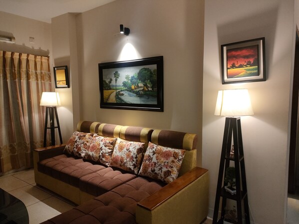 Een woonkamer met een bank, twee vloerlampen, een schilderij en een gordijn.