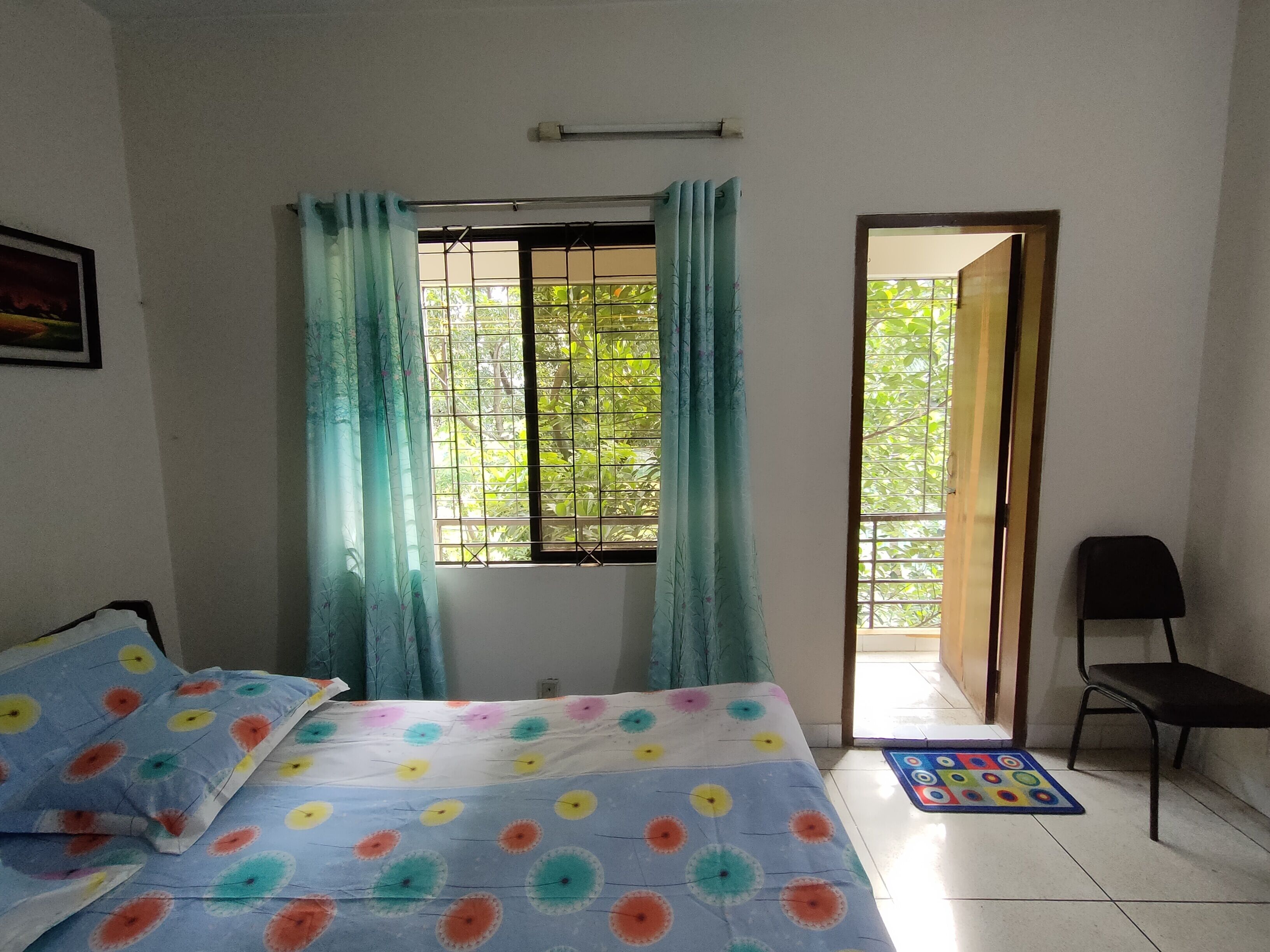 Une chambre à coucher avec un lit, une fenêtre avec des rideaux, une chaise et une porte donnant sur l’extérieur.