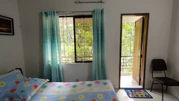 Une chambre à coucher avec un lit, une fenêtre avec des rideaux, une chaise et une porte donnant sur l’extérieur.