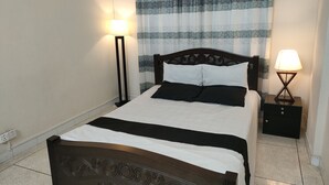 Una cama bien tendida con un cabecero, una mesita de noche con una lámpara y una cortina con estampado geométrico.