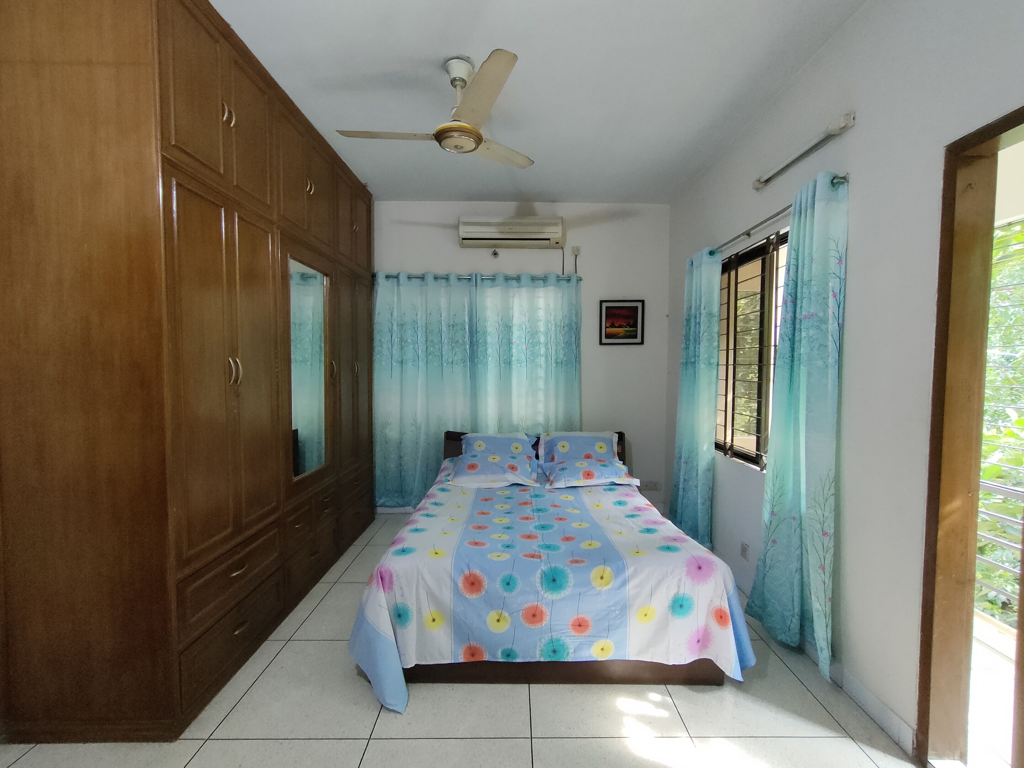 A bedroom with a bed, wardrobe, ceiling fan, air conditioning unit, and curtains.