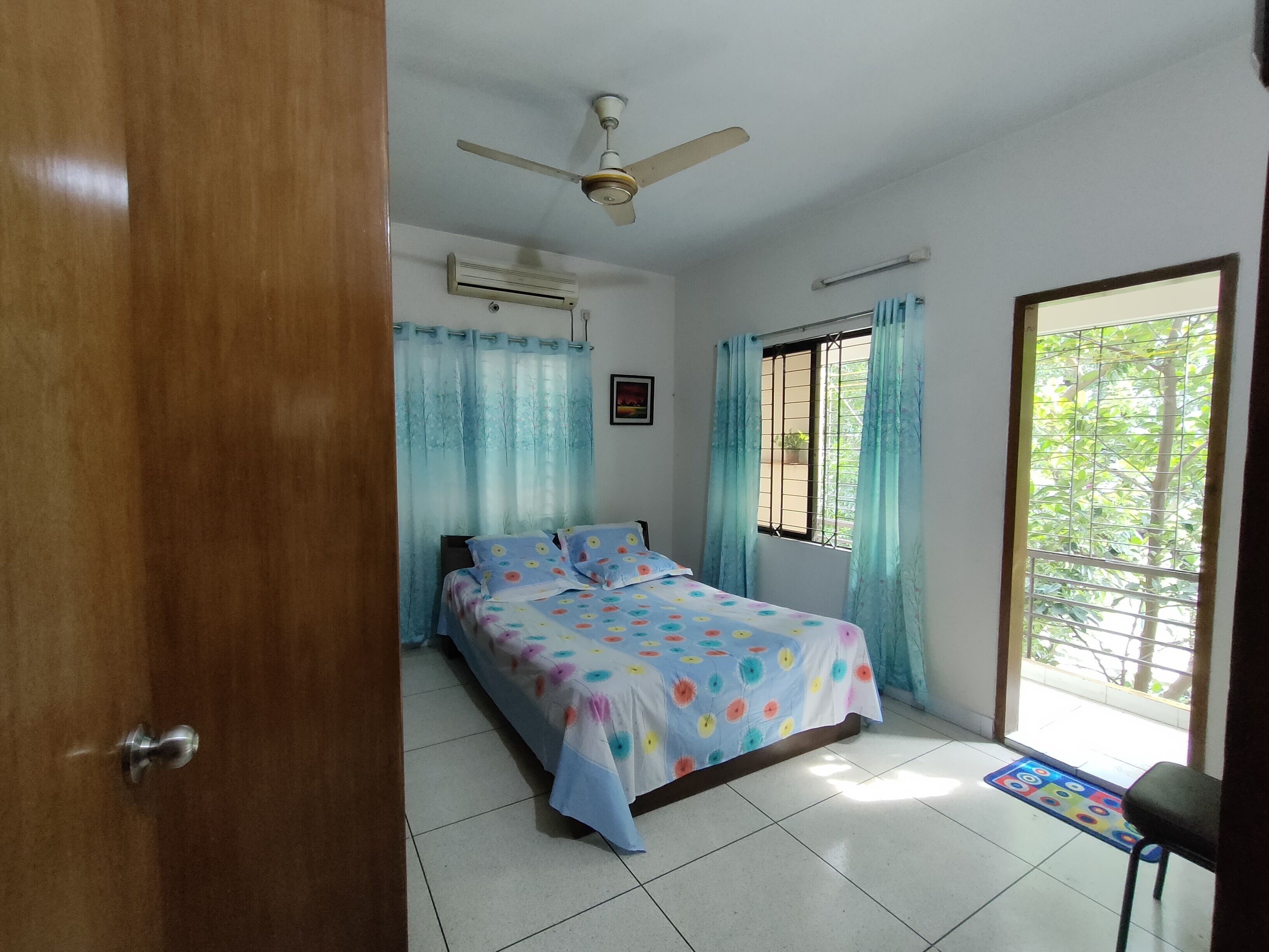 Une chambre à coucher avec un lit, un ventilateur de plafond, une fenêtre avec des rideaux et une porte.