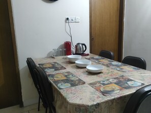 Een eettafel met een bloemen tafelkleed, een waterkoker en verschillende kommen.