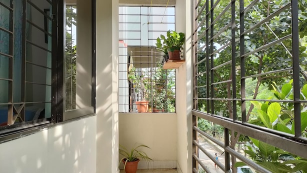 Un balcón con barandilla de metal, una planta en maceta y una ventana con vistas a vegetación.