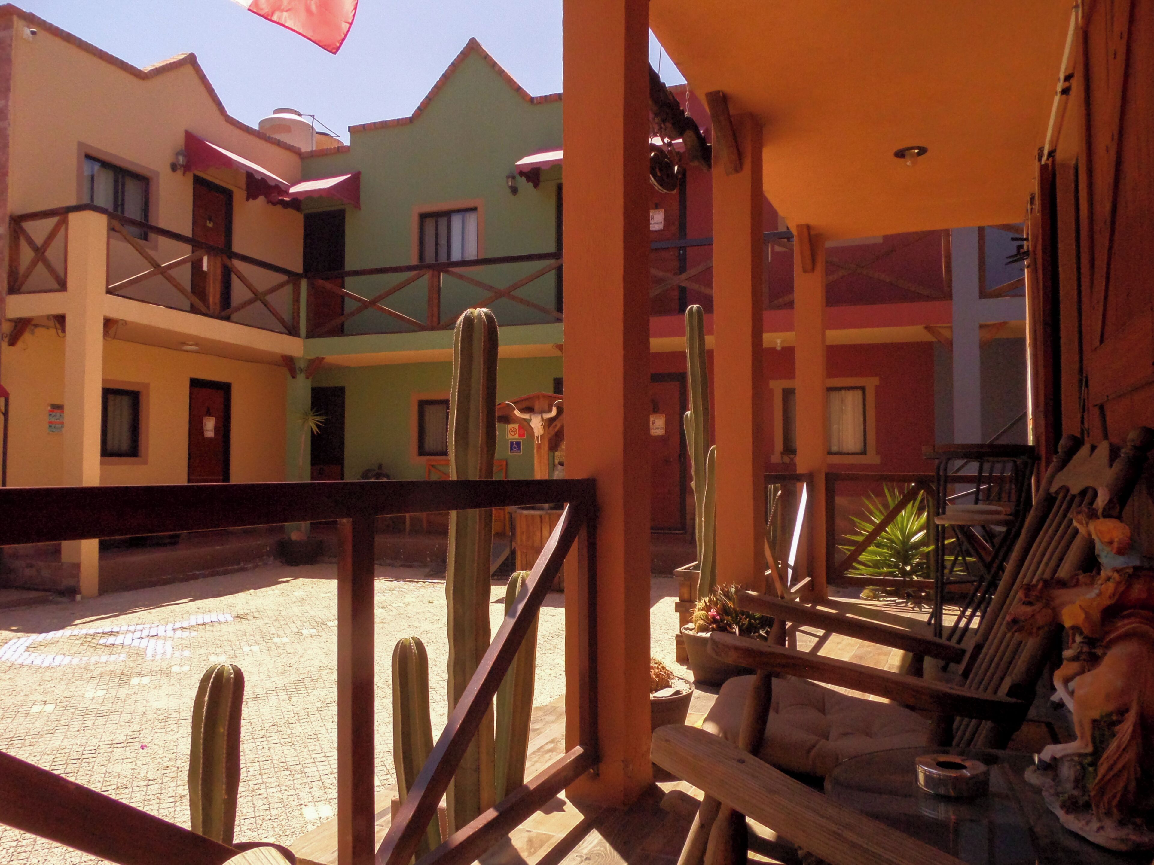 A courtyard with a wooden fence, cacti, and a statue. There are buildings with balconies and windows in the background.
