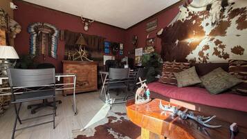 A room with a red couch, a wooden coffee table, a desk, and a chair. There are decorative items on the walls, including a Native American headdress and a cowhide tapestry.