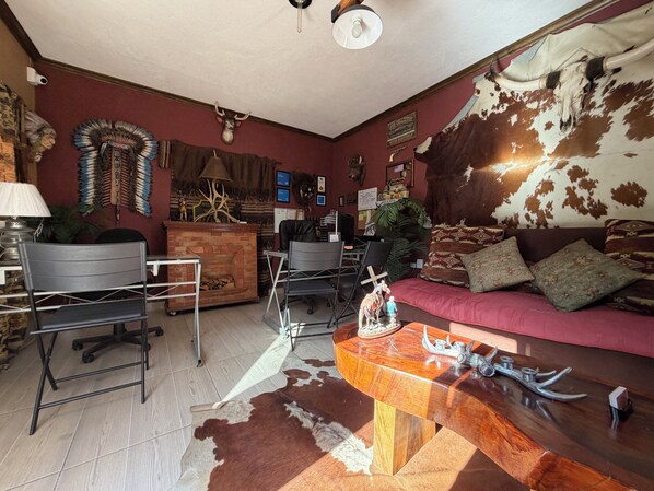 A room with a red couch, a wooden coffee table, a desk, and a chair. There are decorative items on the walls, including a Native American headdress and a cowhide tapestry. - Hotel West Refugio (San Juan del Río)