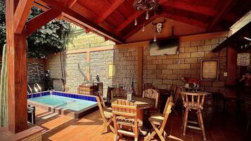Un patio exterior acogedor con pared de piedra, muebles de madera y una pequeña piscina.