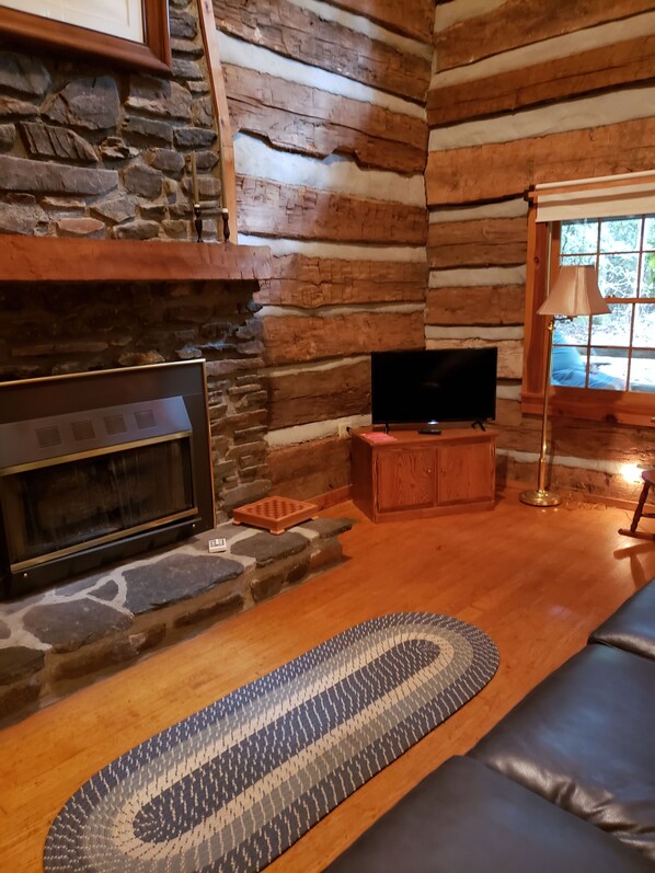 A log cabin interior with a stone fireplace, a television, and a wooden floor.