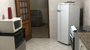A compact kitchen with a microwave, refrigerator, and stove. A wooden door leads to a living area. - Aconchego lar doce lar (Poços de Caldas)