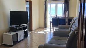 A living room with a flat-screen TV on a stand, a sofa, and a dining area with a table and chairs. - Aconchego lar doce lar (Poços de Caldas)