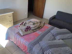Une chambre à coucher avec un lit recouvert de couvertures à motifs, une commode et une porte donnant sur une autre pièce.