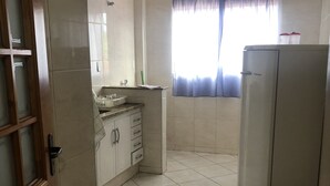 A kitchen with white cabinets, a countertop, a sink, and a refrigerator. - Aconchego lar doce lar (Poços de Caldas)